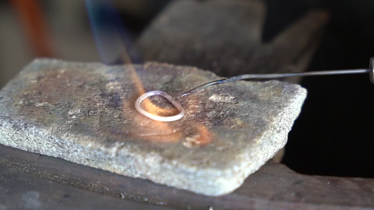 Torch heating and melting precious metal ring for creating an art piece, Close up view