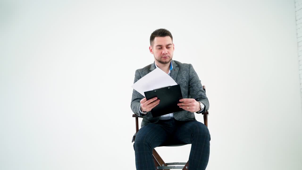 Serious businessman holding a folder and reading documents. Paper works flying over the handsome man in grey suit isolated on white studio background.