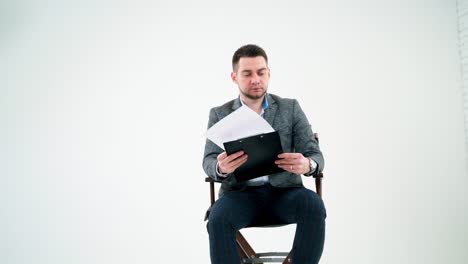serious businessman holding a folder and reading documents. paper works flying over the handsome man in grey suit isolated on white studio background.