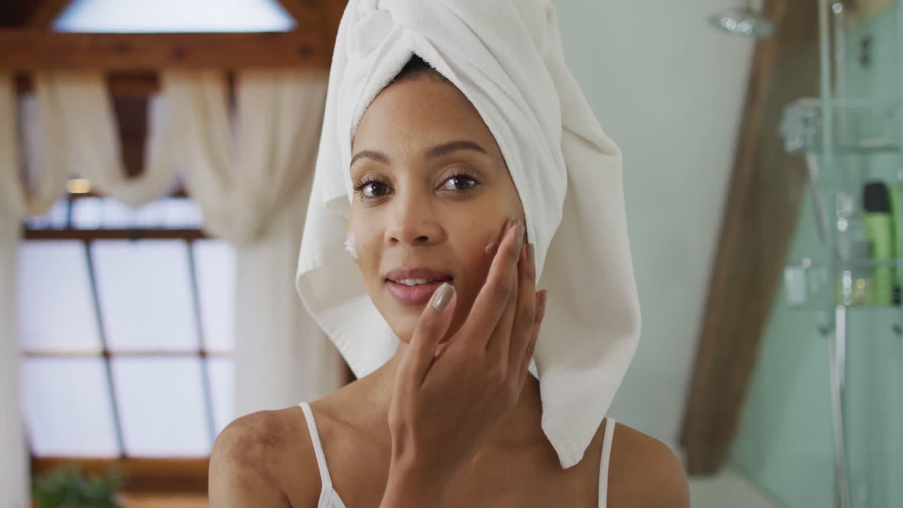 Portrait of mixed race woman wearing towel on head applying cream on her face