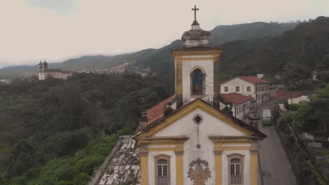 Aerial pan and approach of the facade of Our Lady of Mercy and Charity church in Ouro Preto, Minas Gerais, Brazil, with the Saint Fransisco de Paulo church in the background on an overcast morning