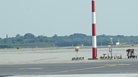 a plane is seen taxiing on an airport runway with a striped pole in the foreground