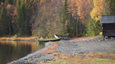 Two-boats-lay-peacefully-on-a-pebble-beach,-surrounded-by-the-vibrant-hues-of-fall-foliage