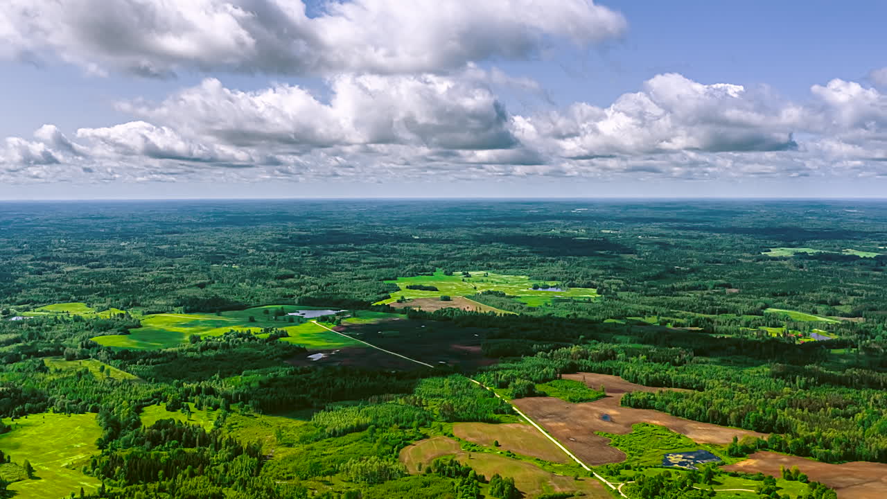 Static aerial wide of fluffy cloud shadows sweeping over fields and trees