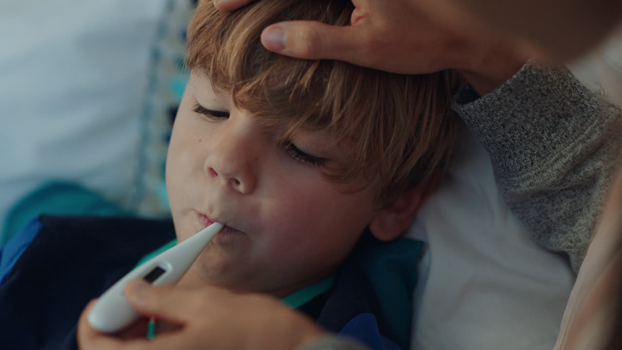 mother caring for sick child lying in bed with flu measuring temperature using thermometer little boy at home with fever mom giving health care