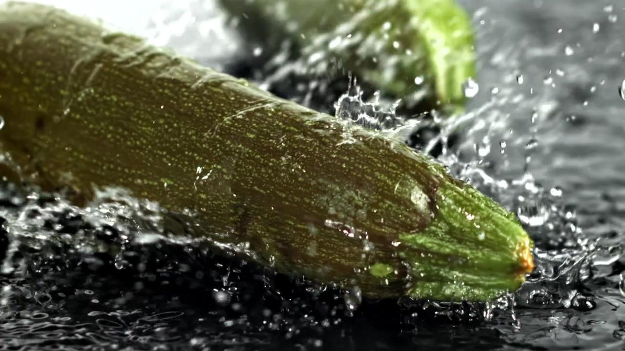 Primo piano di zucchine fresche con acqua che schizza al rallentatore.