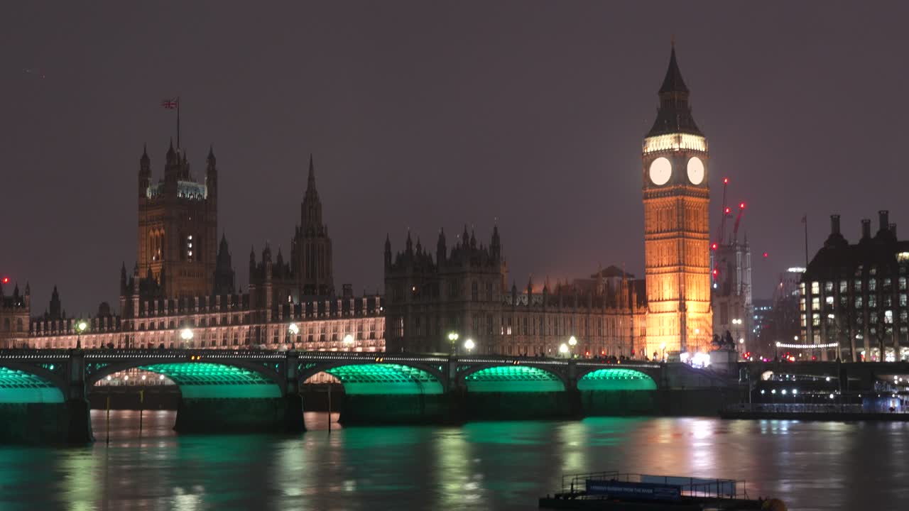 Big Ben og Houses of Parliament i London om natten i timelapse med lys som reflekteres på Themsen. Utsikt som viser Westminster Bridge, opplyste bygninger og bevegelig elvetrafikk