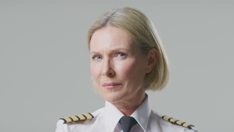 studio portrait of serious mature female airline pilot or ship captain against plain background