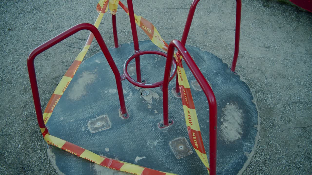 A Slowly Moving Closed Down Merry Go Round Swing in an Empty Kids' Playground Wrapped in Yellow and Red "STOP" Caution Tape due to Quarantine