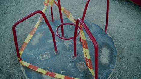 a slowly moving closed down merry go round swing in an empty kids' playground wrapped in yellow and red "stop" caution tape due to quarantine