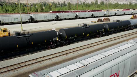 truck-right-drone-shot-flying-over-railroad-station-in-a-desert-environment-on-a-sunny-day-over-black-tank-trains-and-other-cargo-trains