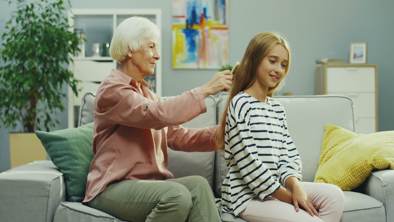거실에 있는 소파에서 10대 손녀의 길고 공정한 머리를 빗고 있는 원로 여성