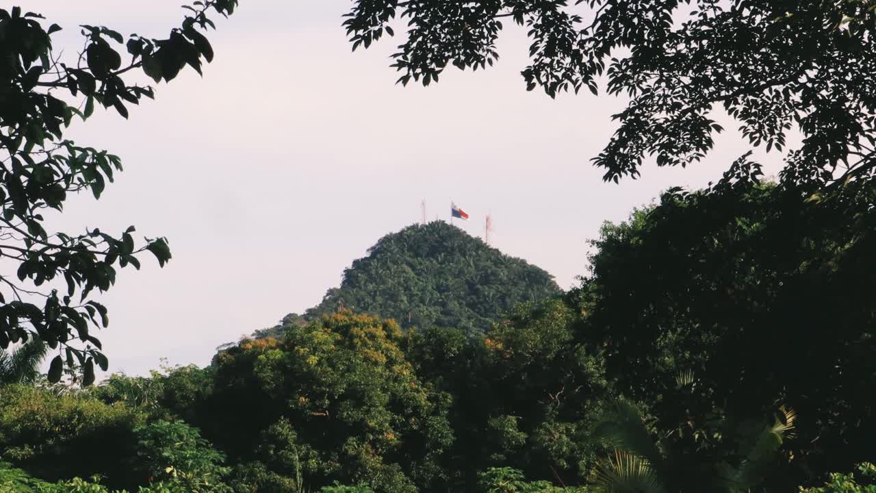 Huge flag of Panama on top of famous Ancon Hill in Panama's Capital City in a beautiful sunny summer morning, viewed from a dense rich green vegetation portraying the inmense biodiversity it has