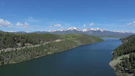 aerial view over the lake surrounded by forest, snowy mountain range of colorado mountains