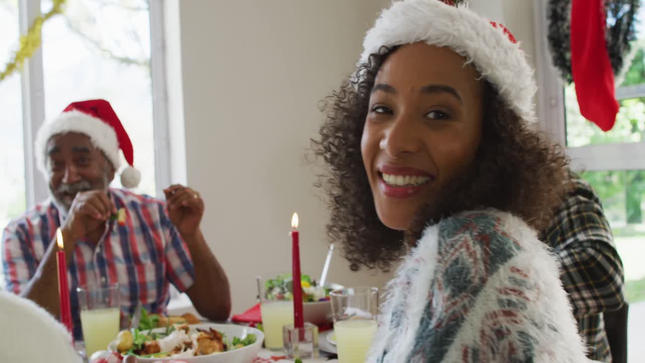 retrato de una mujer afroamericana sonriente con sombrero de santa celebrando la comida navideña con la familia