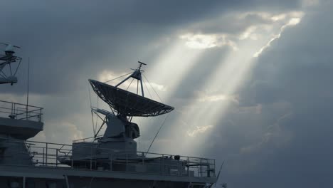 satellite dish on a vessel under dramatic sky with sun rays