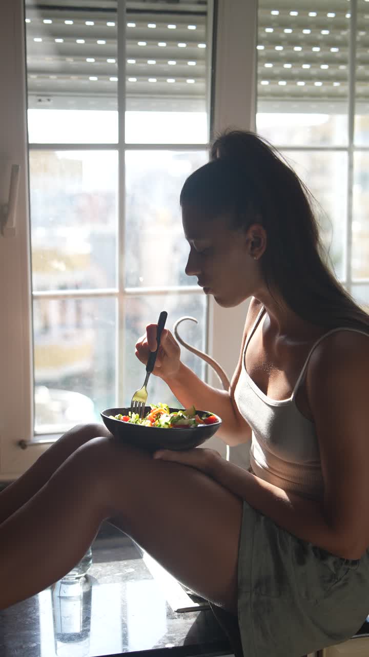 mujer comiendo una ensalada junto a la ventana