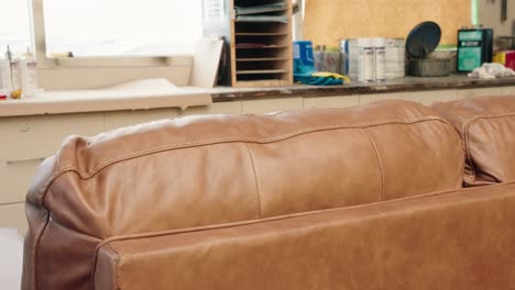 brown leather sofa rests in workshop while technician strolls past in background