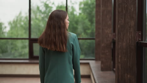 una mujer con una chaqueta verde de pie frente a una ventana