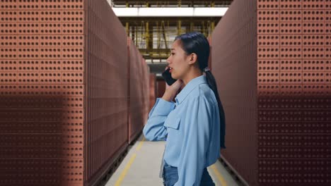 side view asian female with red brick packed in stacks are stored, she pick the phone up and started to specking to it with a slicely smile