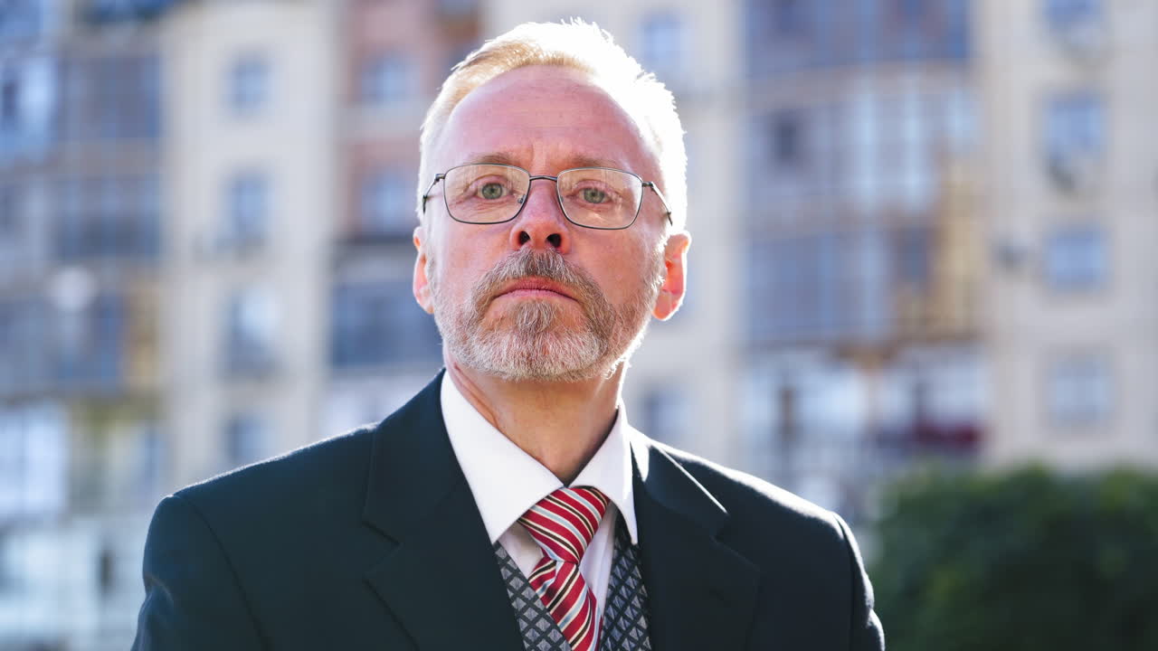 Face of mature businessman in glasses. Middle aged man in elegant costume putting on his eyeglasses and posing to camera outdoors.