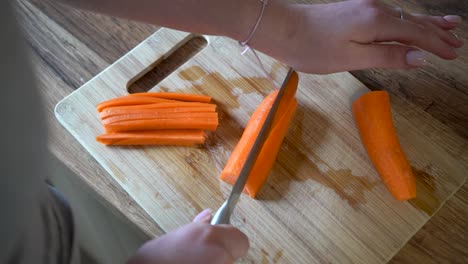 woman cutting carrots with a knife in the kitchen on a wooden cutting board