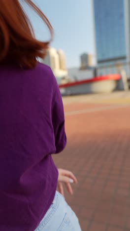 woman wearing purple shirt and light blue jeans, headphones outside in city