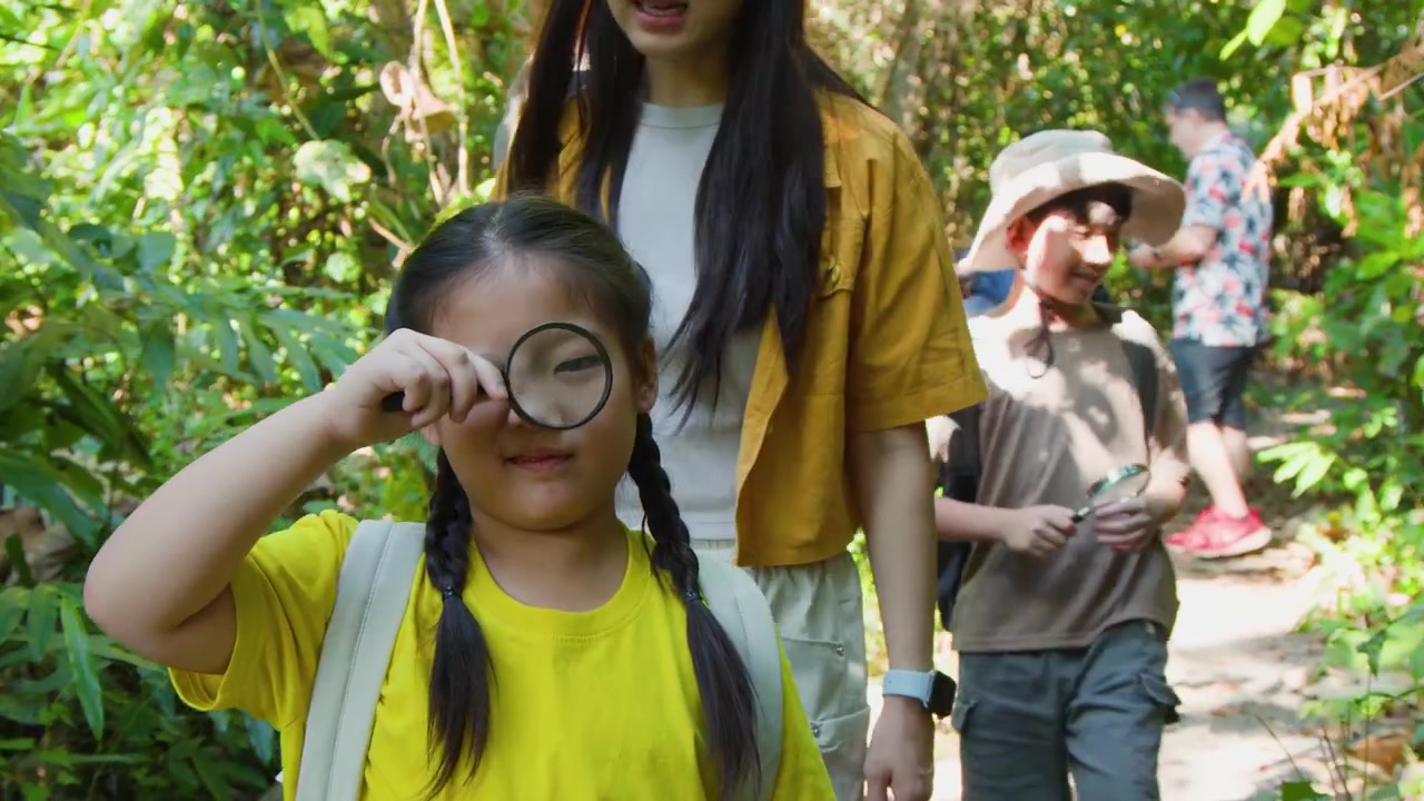 Una giovane ragazza esplora la natura con una lente d'ingrandimento mentre fa un'escursione con la sua famiglia all'aperto.