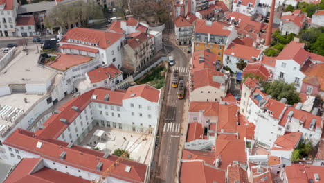 Luftaufnahme-Von-Straßenbahnen,-Die-Auf-Den-Straßen-Der-Stadt-Lissabon-Zwischen-Farbenfrohen-Traditionellen-Häusern-Im-Dichten-Stadtzentrum-Fahren