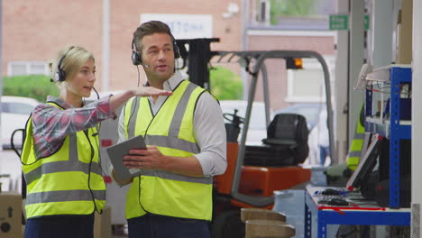 male and female workers wearing headsets in logistics distribution warehouse using digital tablet