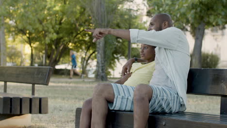 father pointing at something while sitting on bench with his son