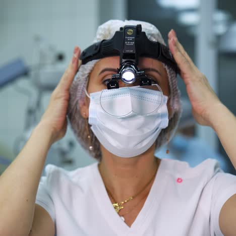 surgeon gets ready before operation. pretty woman puts on special lamp on head and loupe. ophthalmology operation in modern clinic