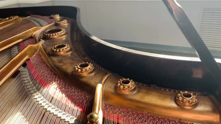 Camera moving under the opened lid of a classic older grand piano showing piano strings and stopping in front of piano keys.