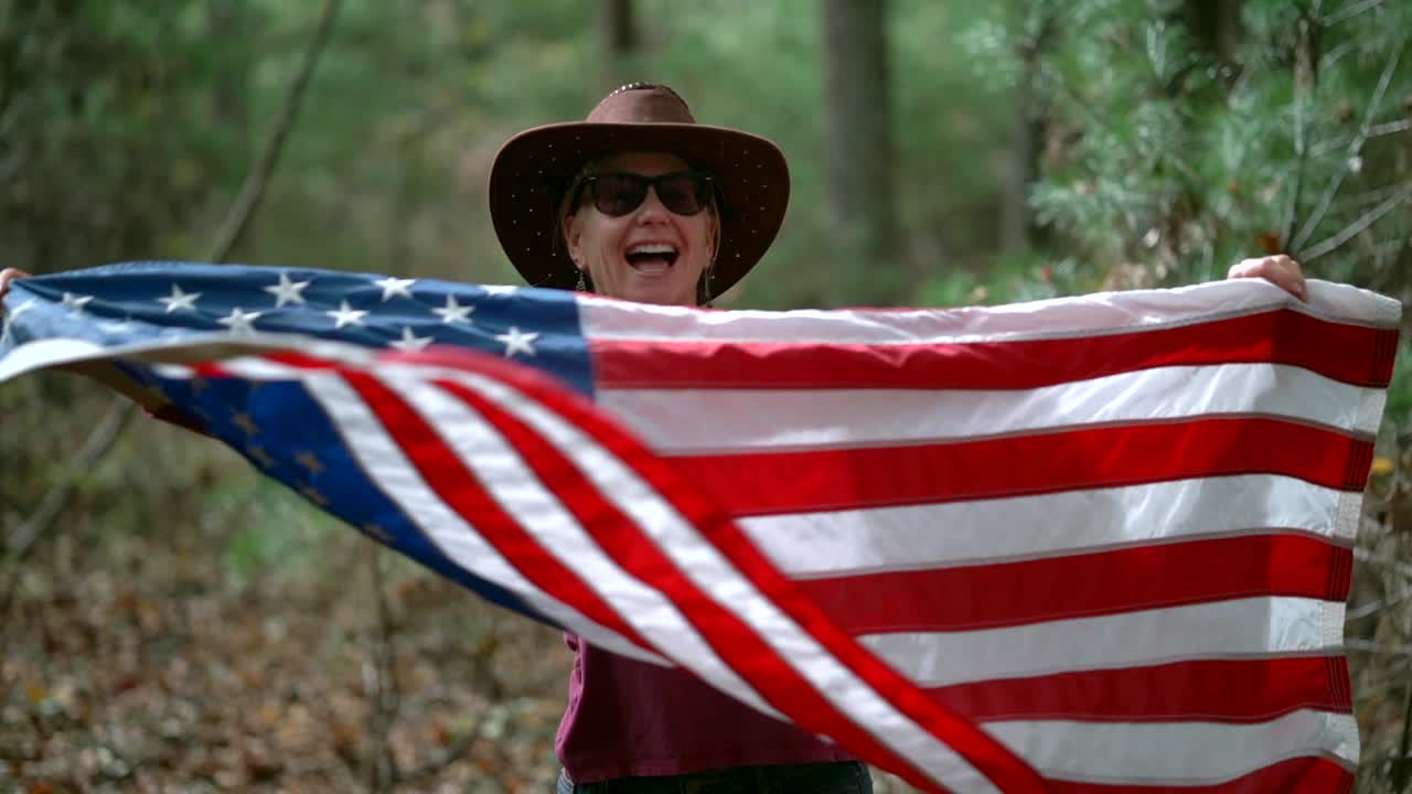 movimiento lento de la mujer en sombrero de vaquero y bandera azotar una bandera alrededor mientras sonríe y ríe