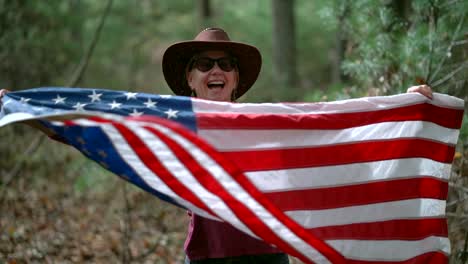 slow motion of woman in cowboy hat and flag whip a flag around while smiling and laughing