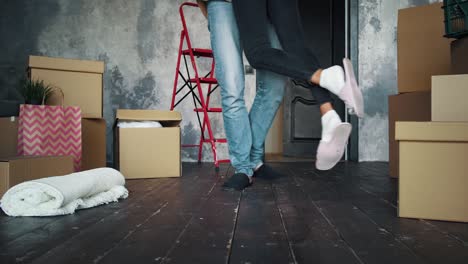 spouses in slippers, relocating into new house. male raising and circling female, being in room with cardboard boxes and packages. slow motion