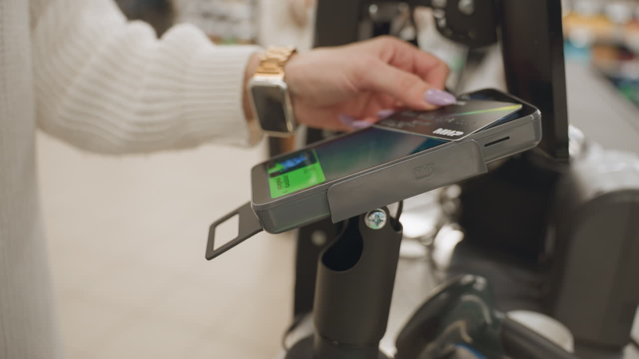 Close up of shopper hand with manicured nails holding metallic payment card over contactless payment reader at supermarket checkout tapping card for purchase transaction in retail environment