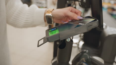 close up of shopper hand with manicured nails holding metallic payment card over contactless payment reader at supermarket checkout tapping card for purchase transaction in retail environment