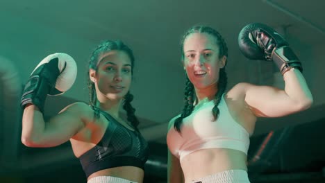 two smiling female boxers in braided pigtails looking at the camera and showing biceps