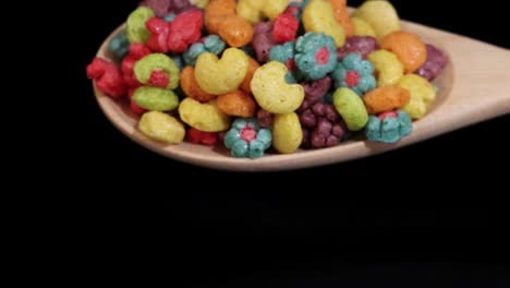 vibrant cereal pieces tumble from a wooden spoon against a black background, creating a dynamic and colorful scene