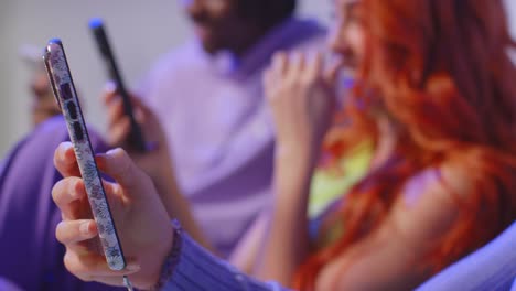 close up studio shot of young gen z friends sitting on sofa talking and sharing social media post on mobile phones 10