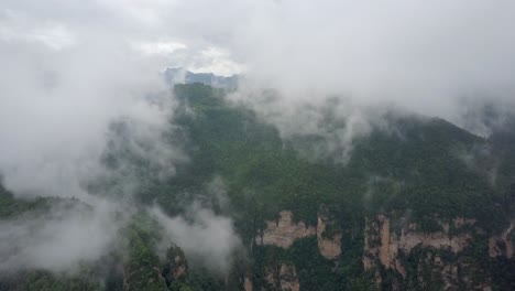 Cloud-aerial-in-Chinese-forest-valley-with-steep-rocky-spires,-cliffs
