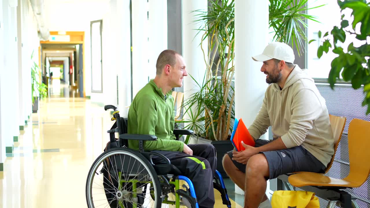 Two men talking in a hallway, one in a wheelchair
