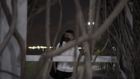 view across tree branches of man wearing a black mask carrying a guitar during corona virus