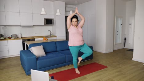 Mujer-Regordeta-Realizando-Asanas-De-Yoga-En-Casa-Con-Un-Tutor-En-Línea-En-Una-Computadora-Portátil