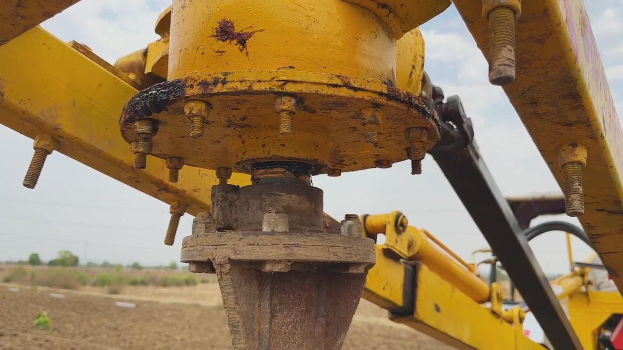 Vista ravvicinata della testa motrice della trivella e del gruppo di montaggio che girano mentre la trivella penetra nel terreno per la recinzione, con bulloni metallici e meccanismo visibili in un ambiente rurale all'aperto.
