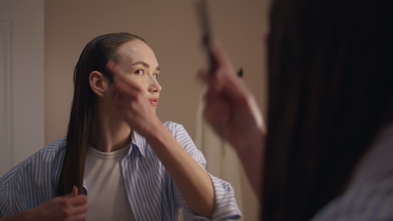 Smiling lady comb hair at home. Pretty girl getting ready in mirror reflection