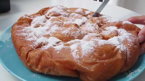 freshly baked chocolate-filled ensaimada topped with powdered sugar on a blue plate