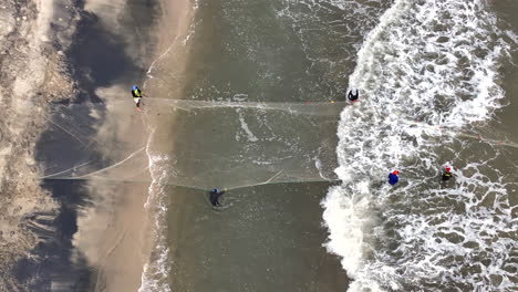 aerial shot fishermen pulling fishing net from ocean sand beach colombia waves