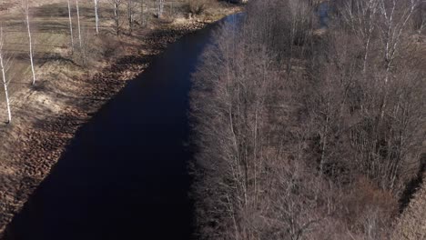 aerial footage of mystical black river in sweden surrounded by trees and fields